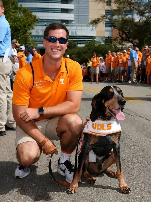 Dr. Harlan kneeling beside a hound in a Vols vest on a UT game day