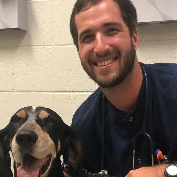 Dr. Matthew Harlan smiling beside a hound in an exam room