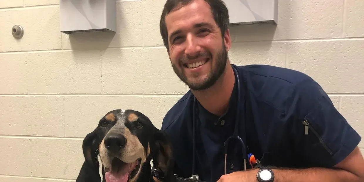 Dr. Matthew Harlan smiling beside a hound in an exam room