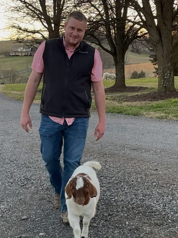 Dr. Harris walking with a young Boer goat down a gravel farm drive